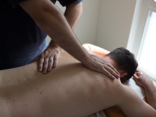 Therapeut behandelt Nacken und Schulter eines liegenden Patienten.