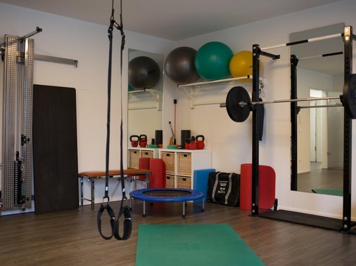 Trainingsraum mit Zugapparaten, Gymnastikbällen, Kettlebells und Kniebeugen-Rack.