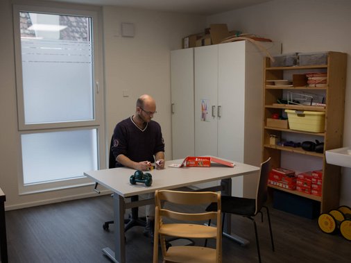 Mann sitzt am Tisch mit Therapiematerial in einem Ergotherapie-Raum.