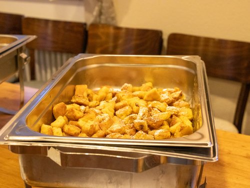 Schale mit gebackenen, mit Puderzucker bestreuten Teigstücken (Kaiserschmarrn) auf dem Buffet.