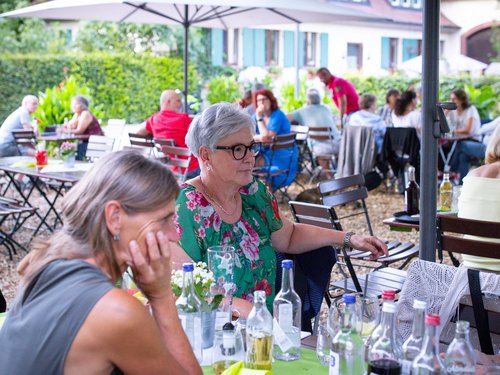 Gruppe von Kolleg:innen sitzt an einem langen Tisch im Freien, Getränkeflaschen im Vordergrund.