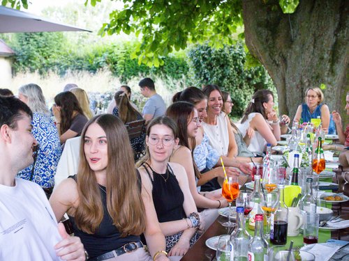 Große Gruppe von Kolleg:innen sitzt gemeinsam an einer langen Tafel im Freien.