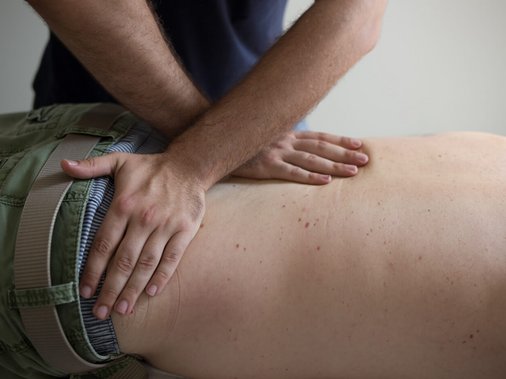 Therapeutin unterstützt einen Patienten bei einer Übung am Kabelzug-Trainingsgerät, im Hintergrund Tür „Gymnastik".