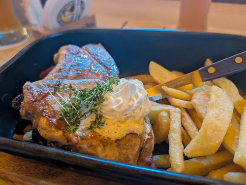Schweinebraten mit Kartoffelspalten, Kräuter-Sahne-Topping und Pommes in einer Servierpfanne.