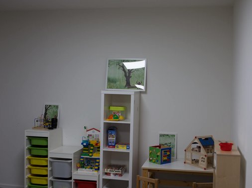 Kinder-Ergotherapieraum mit bunten Aufbewahrungsboxen, Spielhaus, Bausteinen und Sitzkissen.
