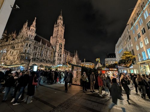 Marienplatz in München bei Nacht während der Weihnachtsmarktzeit, beleuchtetes Rathaus und Besucher.