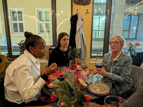 Kolleginnen sitzen an einem weihnachtlich dekorierten Tisch mit Rotwein und Brot.