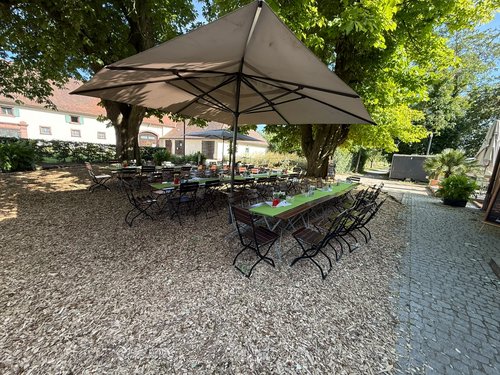 Leere, festlich gedeckte Tischreihen unter großen Sonnenschirmen im Garten eines Guts.