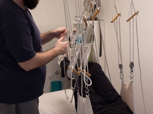 Therapeut befestigt Schlingen einer Extensionsvorrichtung an den Beinen eines liegenden Patienten.