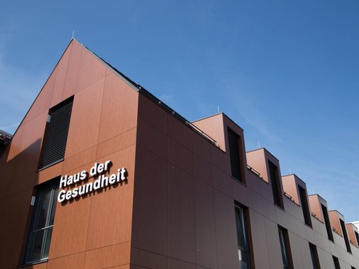 Gebäudefassade „Haus der Gesundheit" in Cortenstahl-Optik vor blauem Himmel.