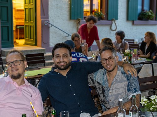 Drei Männer posieren lächelnd mit den Armen umeinander bei der abendlichen Feier.