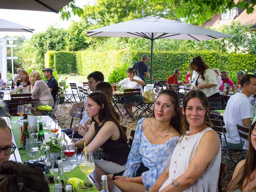 Drei Frauen sitzen lächelnd zusammen an einer langen Tafel im Freien.