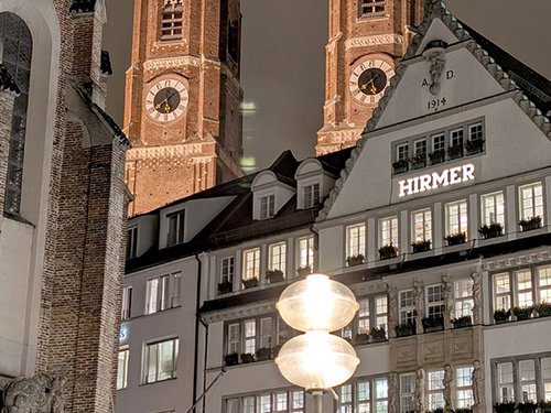 Die Frauenkirche mit ihren markanten Zwiebeltürmen bei Nacht, im Vordergrund das Kaufhaus Hirmer.