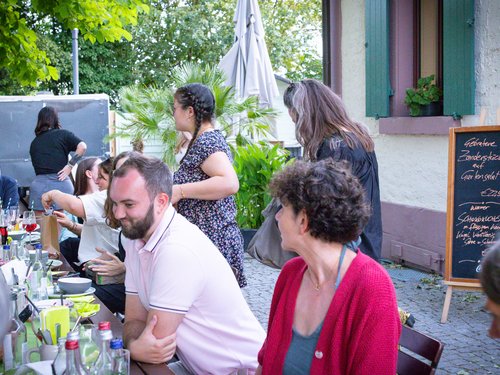 Kolleg:innen sitzen an einer langen Tafel, im Hintergrund eine Speisekarte mit Angeboten.